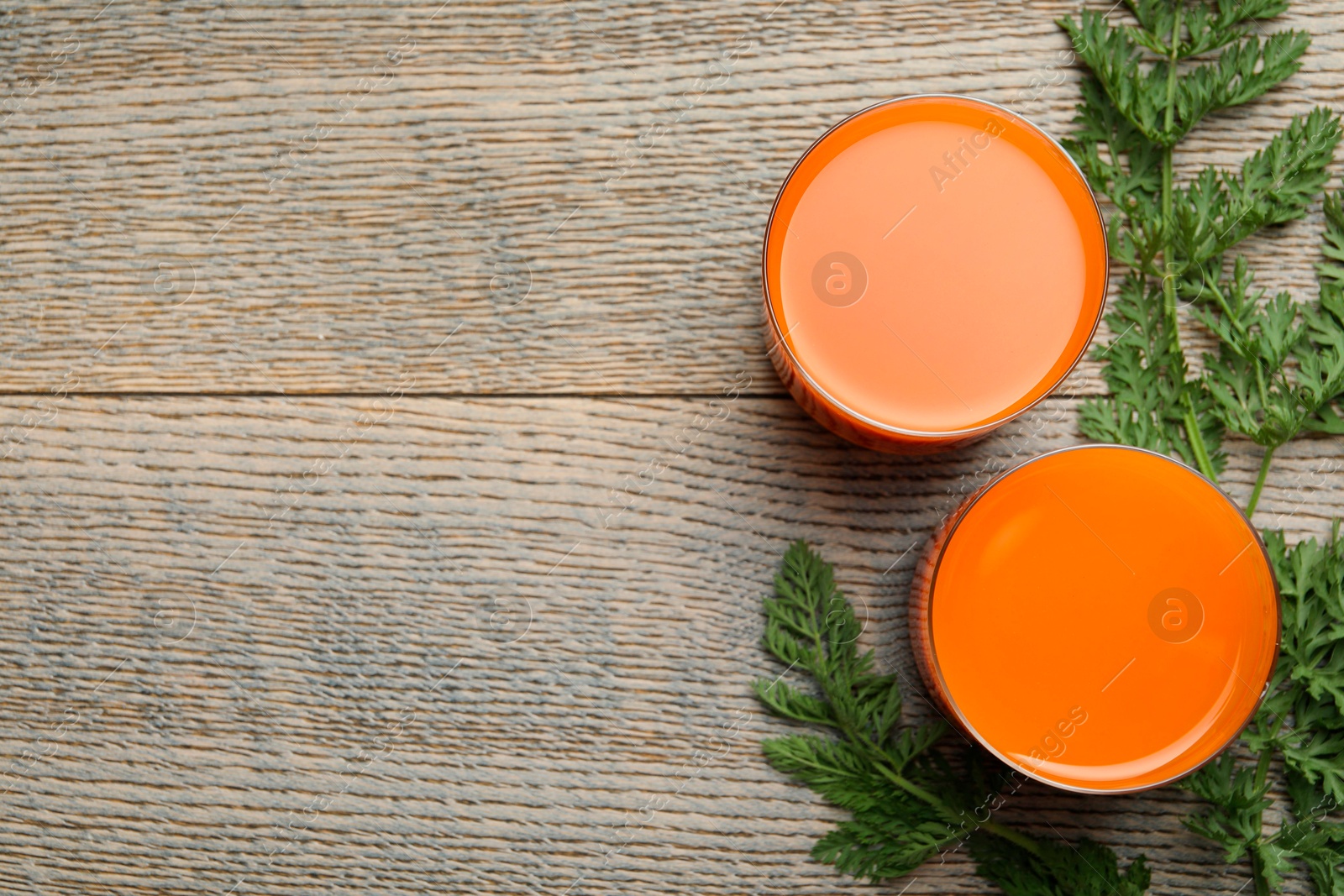 Photo of Healthy carrot juice in glasses and green leaves on wooden table, top view. Space for text