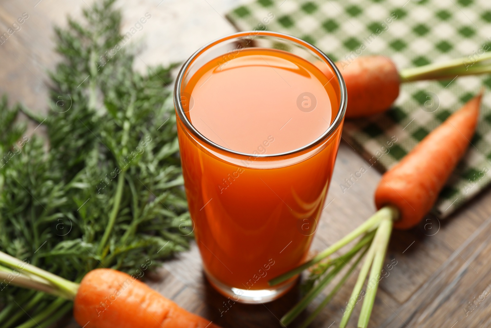 Photo of Healthy carrot juice in glass and fresh vegetables on wooden table