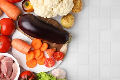 Different vegetables and raw meat for stew on white tiled table, top view. Space for text