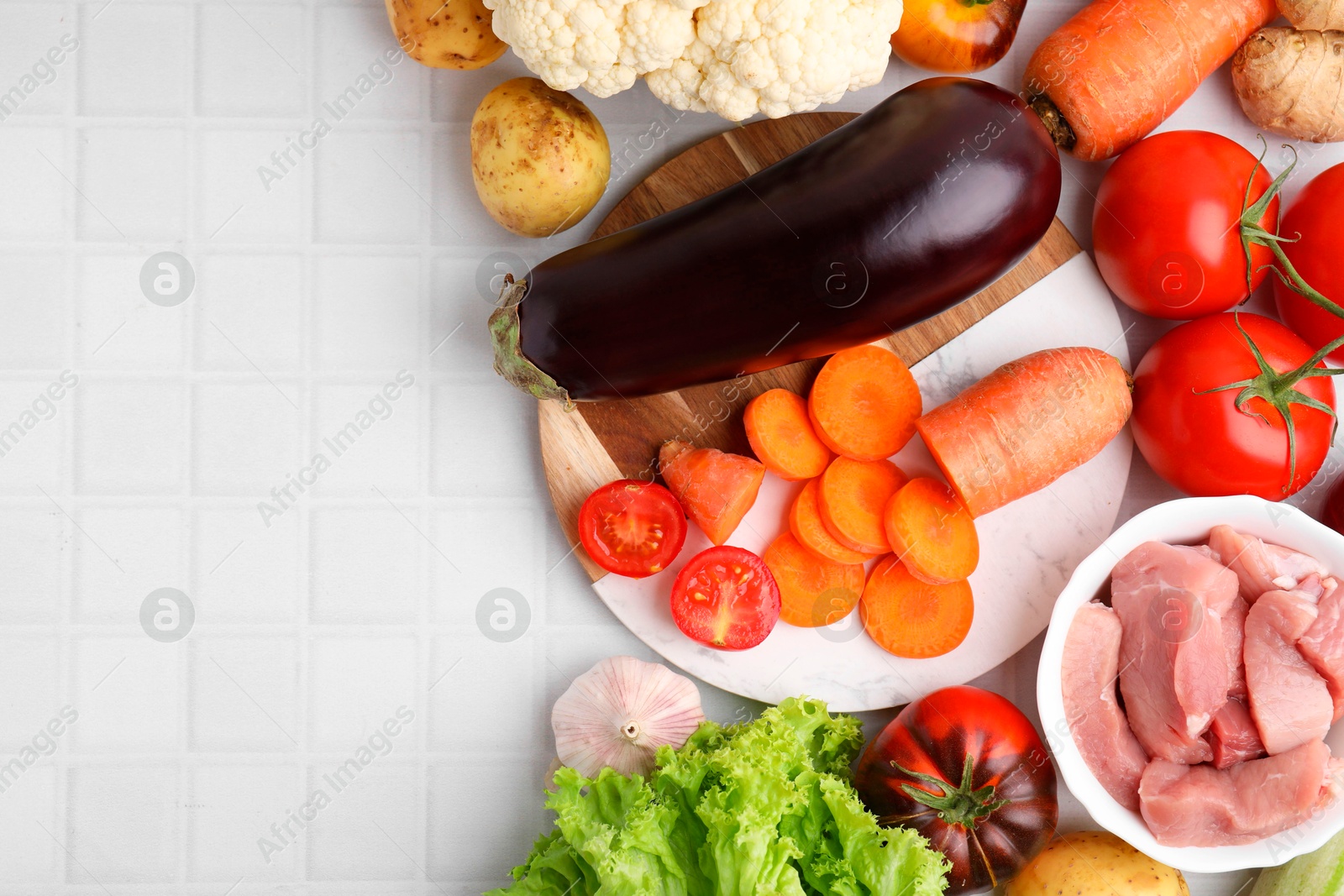 Photo of Different vegetables and raw meat for stew on white tiled table, top view. Space for text