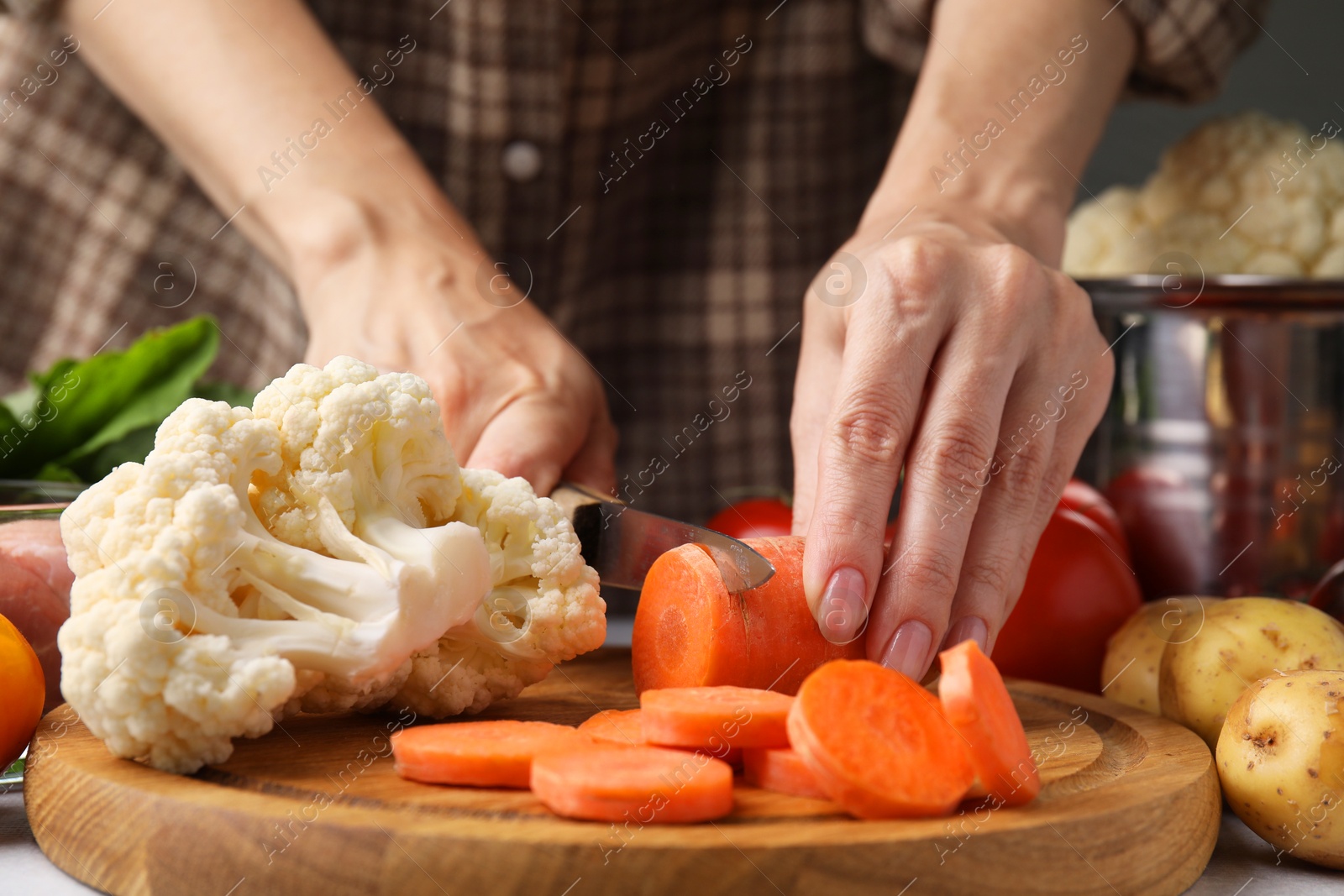 Photo of Cooking vegetable stew. Woman cutting carrot at table, closeup