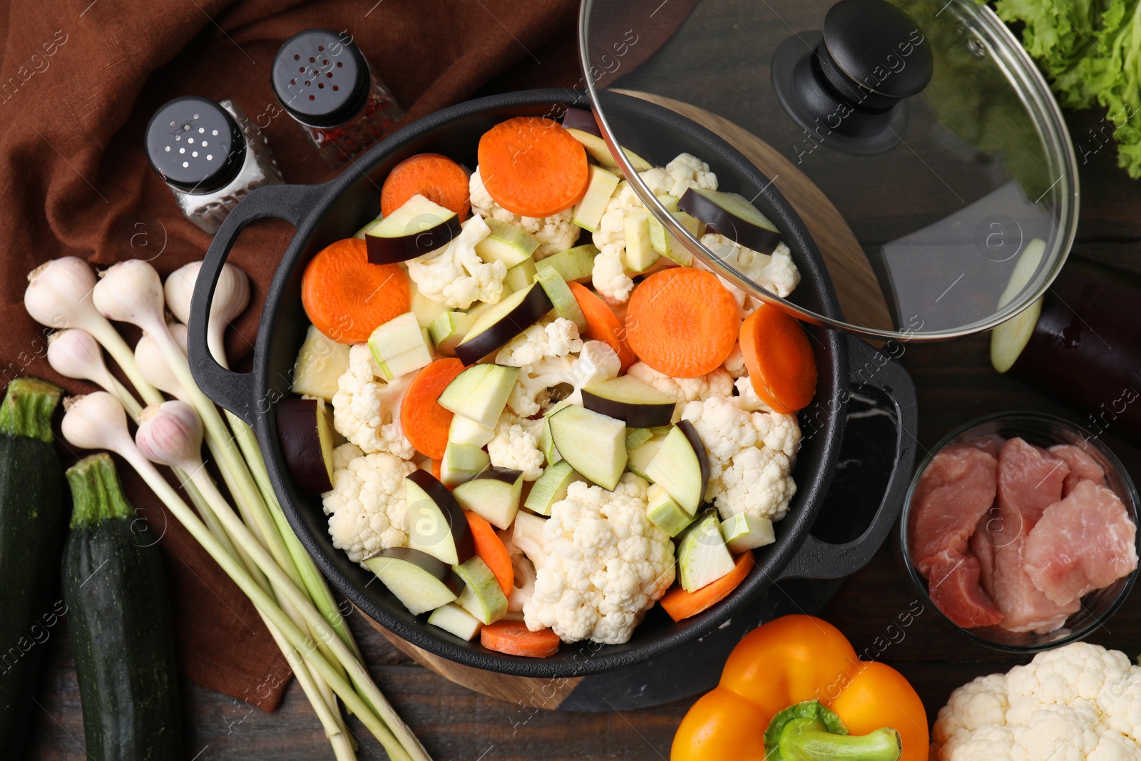 Photo of Cooking stew. Cut raw vegetables in pot and meat on wooden table, flat lay