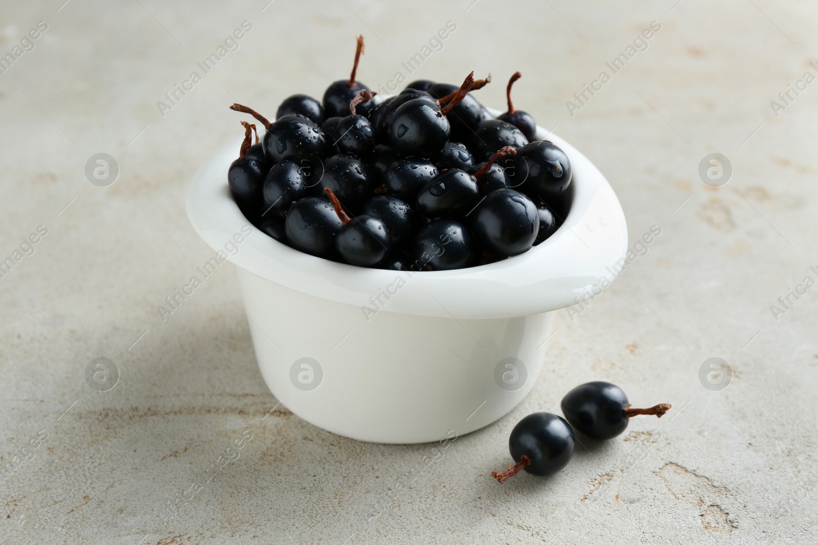 Photo of Ripe black currants in bowl on light table, closeup