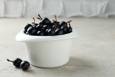 Ripe black currants in bowl on light table. Space for text