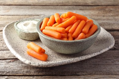 Baby carrots in bowl and sauce on wooden table