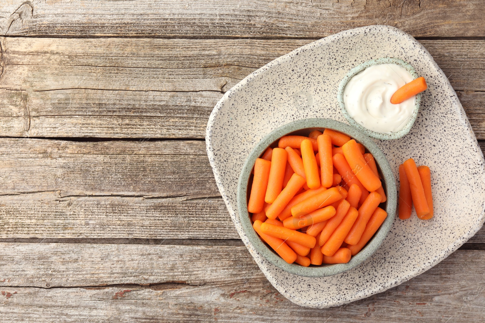 Photo of Baby carrots in bowl and sauce on wooden table, top view. Space for text