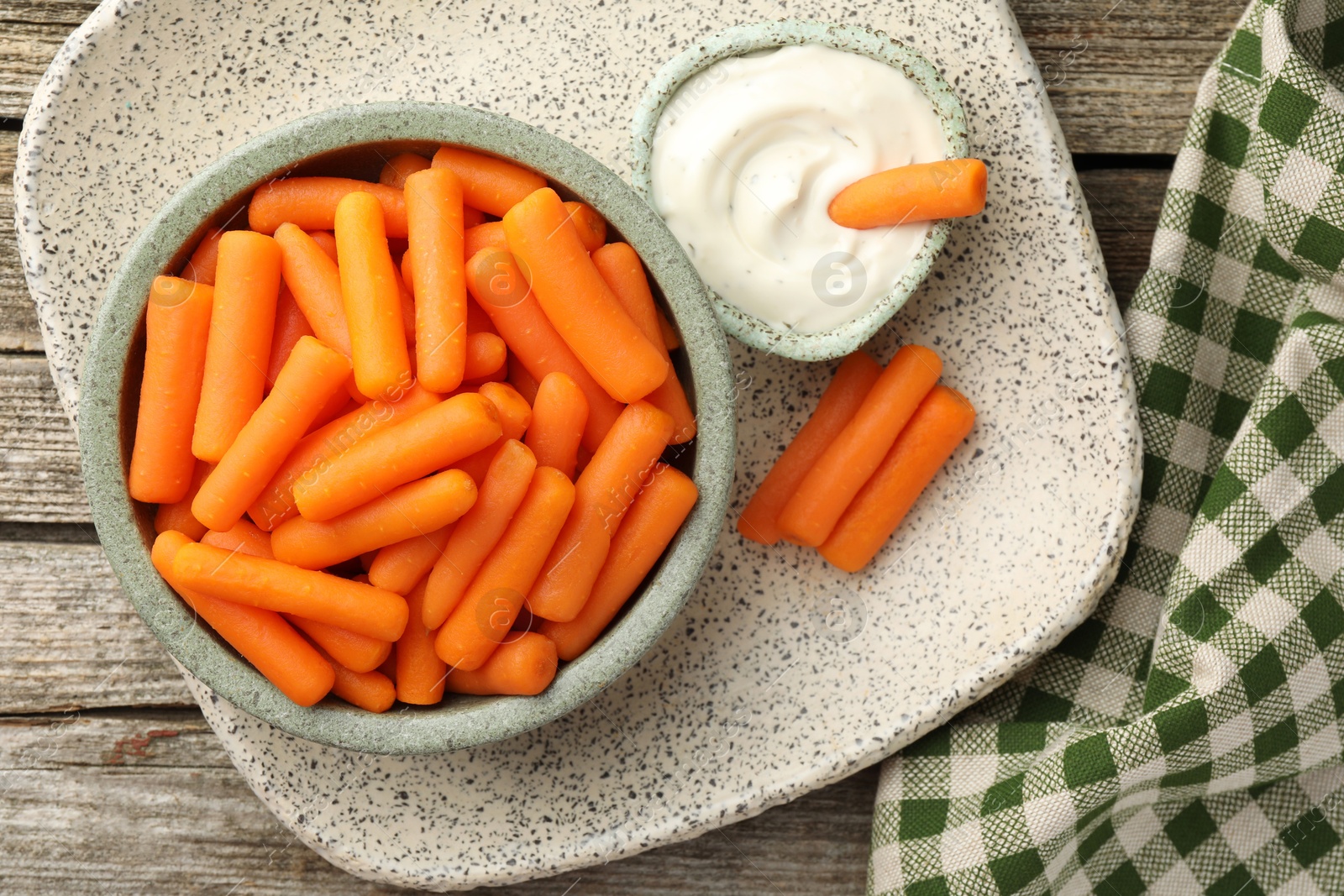 Photo of Baby carrots in bowl and sauce on wooden table, top view