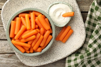 Baby carrots in bowl and sauce on wooden table, top view