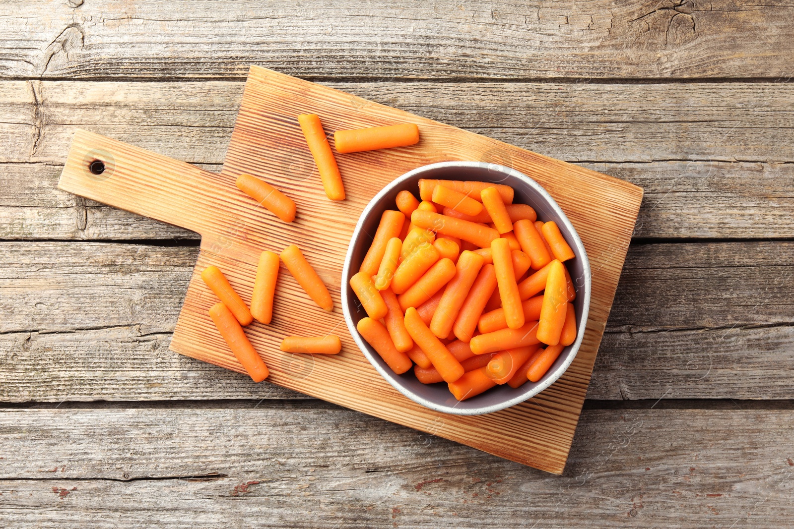 Photo of Baby carrots in bowl on wooden table, top view