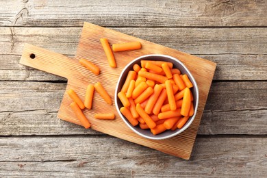 Photo of Baby carrots in bowl on wooden table, top view