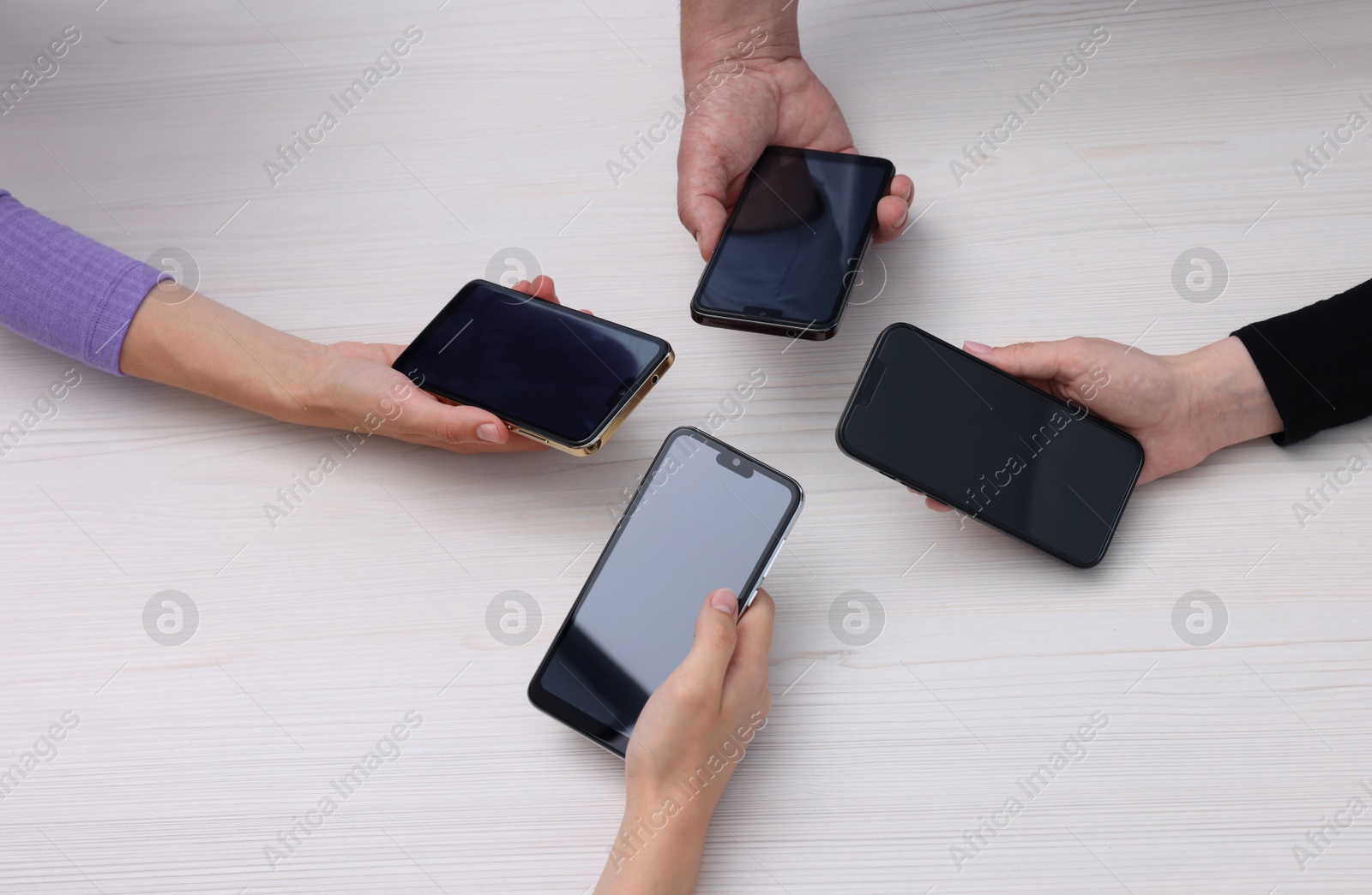 Photo of People holding smartphones with blank screens at white wooden table, closeup. Mockup for design