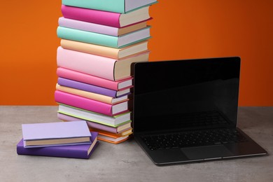 Stack of colorful books and laptop on wooden table against orange background