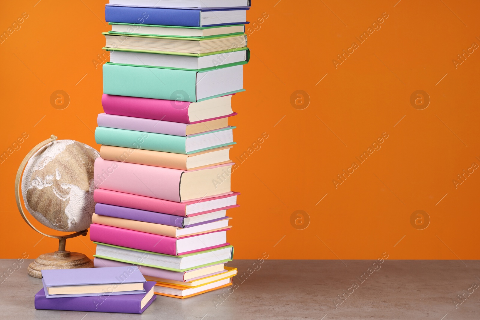 Photo of Stack of colorful books and globe on wooden table against orange background, space for text