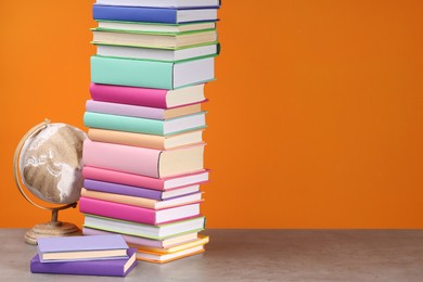 Photo of Stack of colorful books and globe on wooden table against orange background, space for text