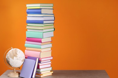 Photo of Stack of colorful books and globe on wooden table against orange background, space for text