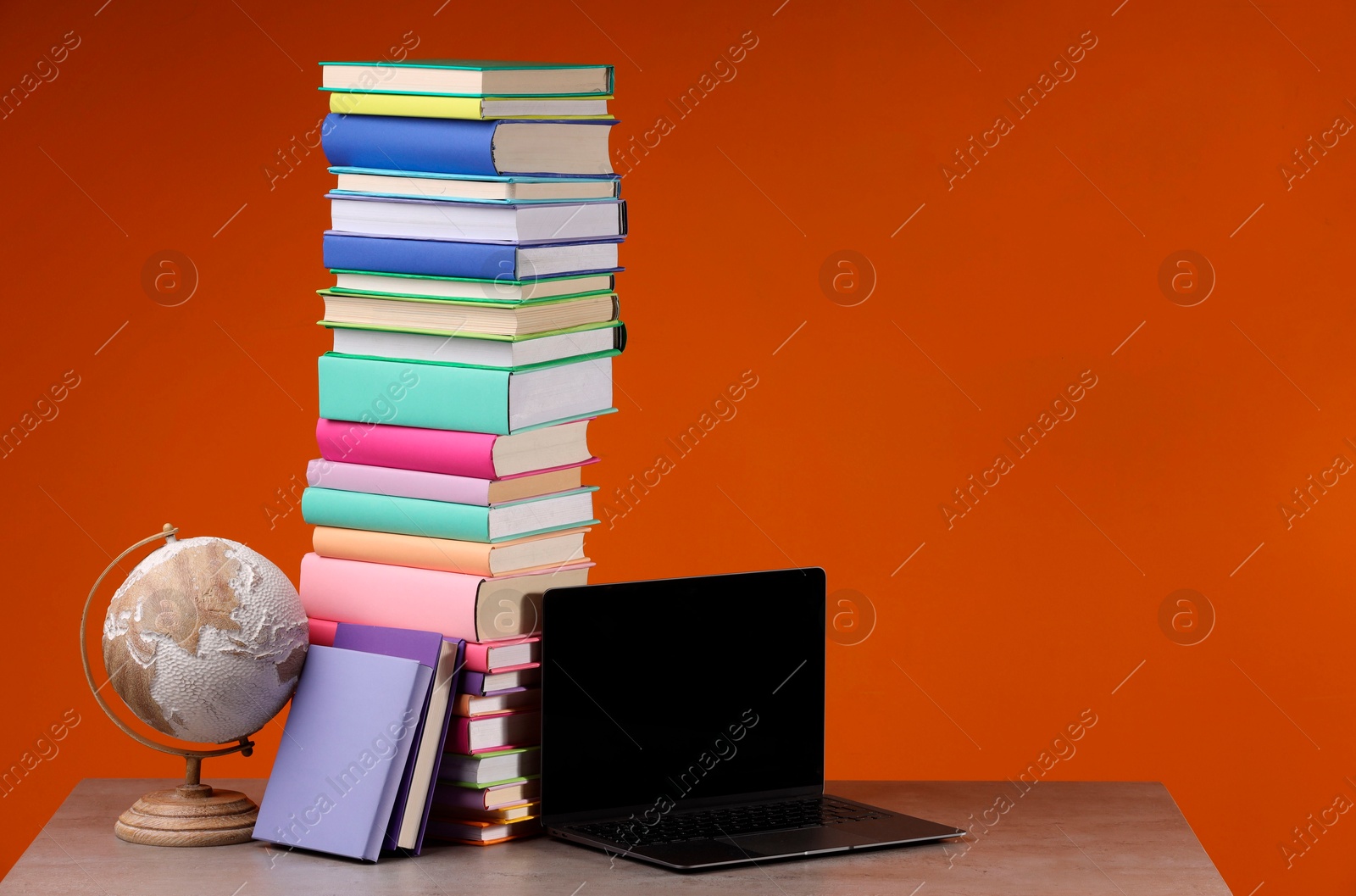 Photo of Stack of colorful books, globe and laptop on wooden table against orange background, space for text