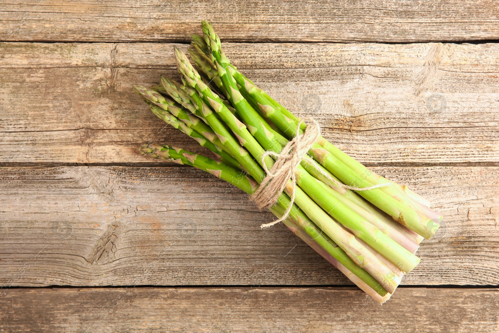 Photo of Bunch of fresh green asparagus stems on wooden table, top view