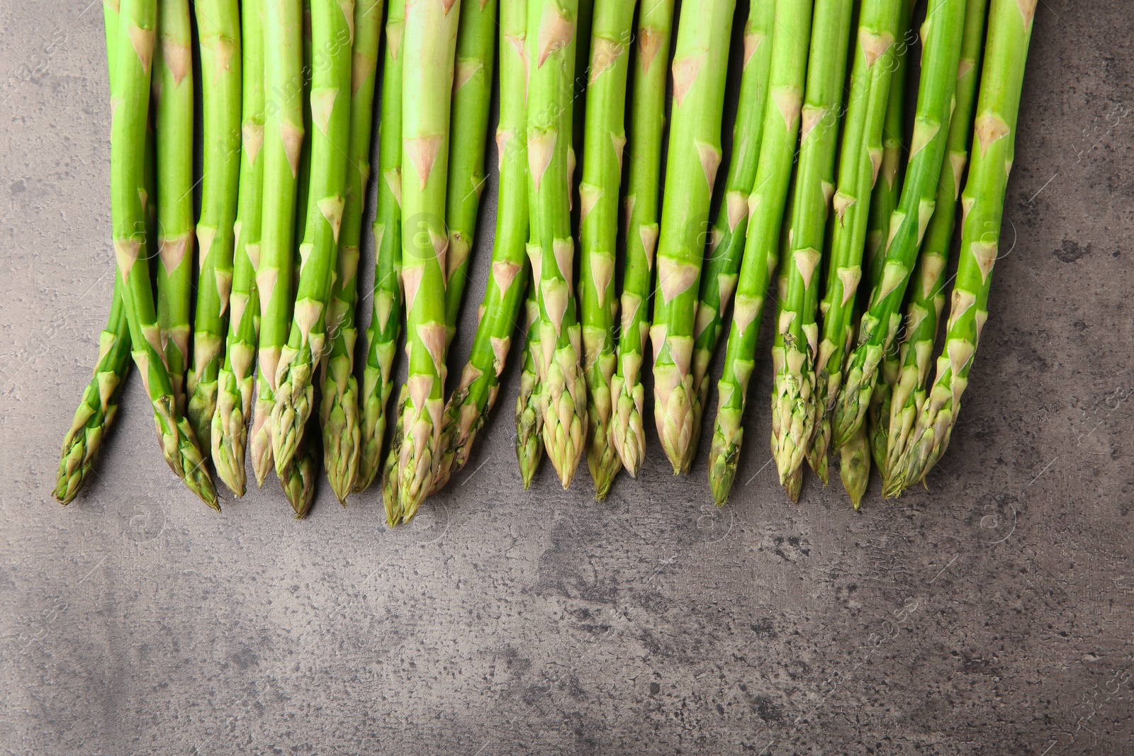 Photo of Fresh green asparagus stems on grey textured table, flat lay. Space for text