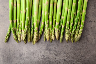 Fresh green asparagus stems on grey textured table, flat lay. Space for text