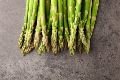 Fresh green asparagus stems on grey textured table, flat lay. Space for text