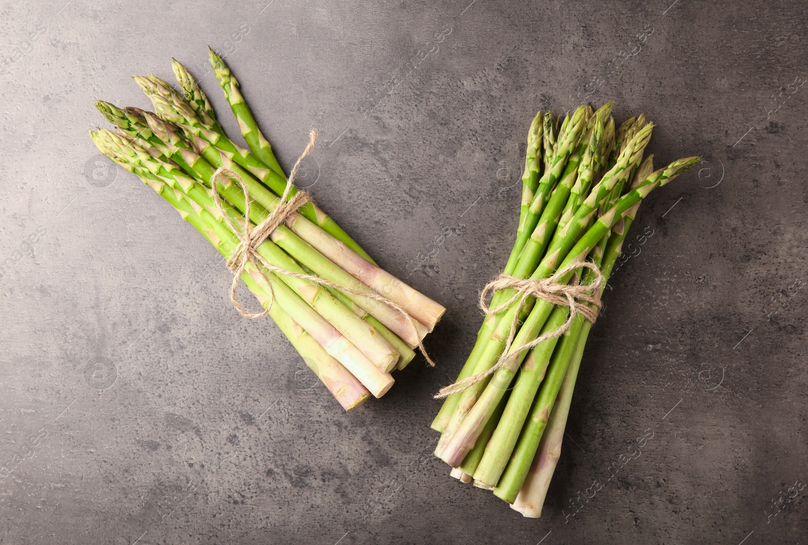 Photo of Bunches of fresh green asparagus stems on grey textured table, flat lay