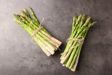 Bunches of fresh green asparagus stems on grey textured table, flat lay