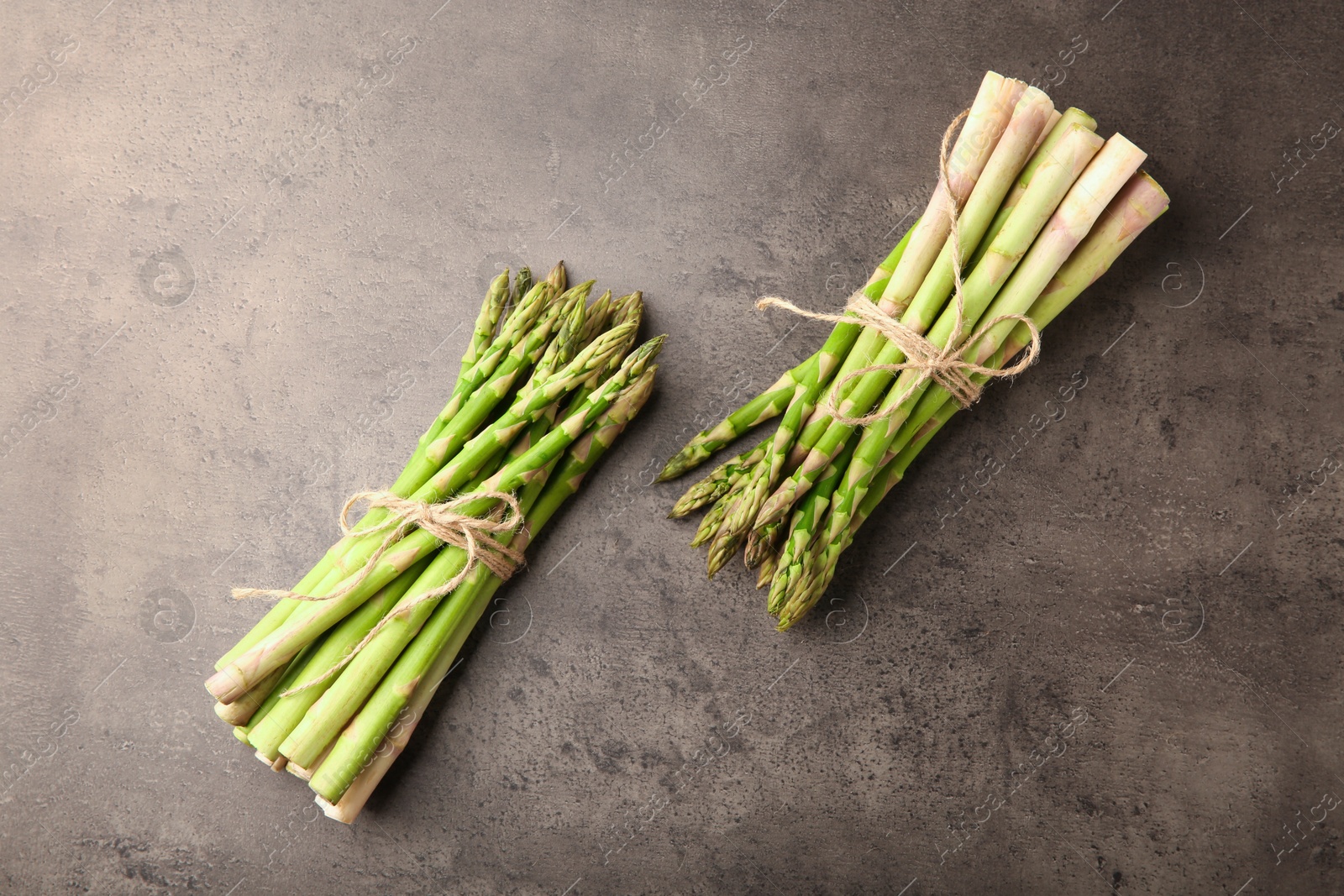 Photo of Bunches of fresh green asparagus stems on grey textured table, flat lay