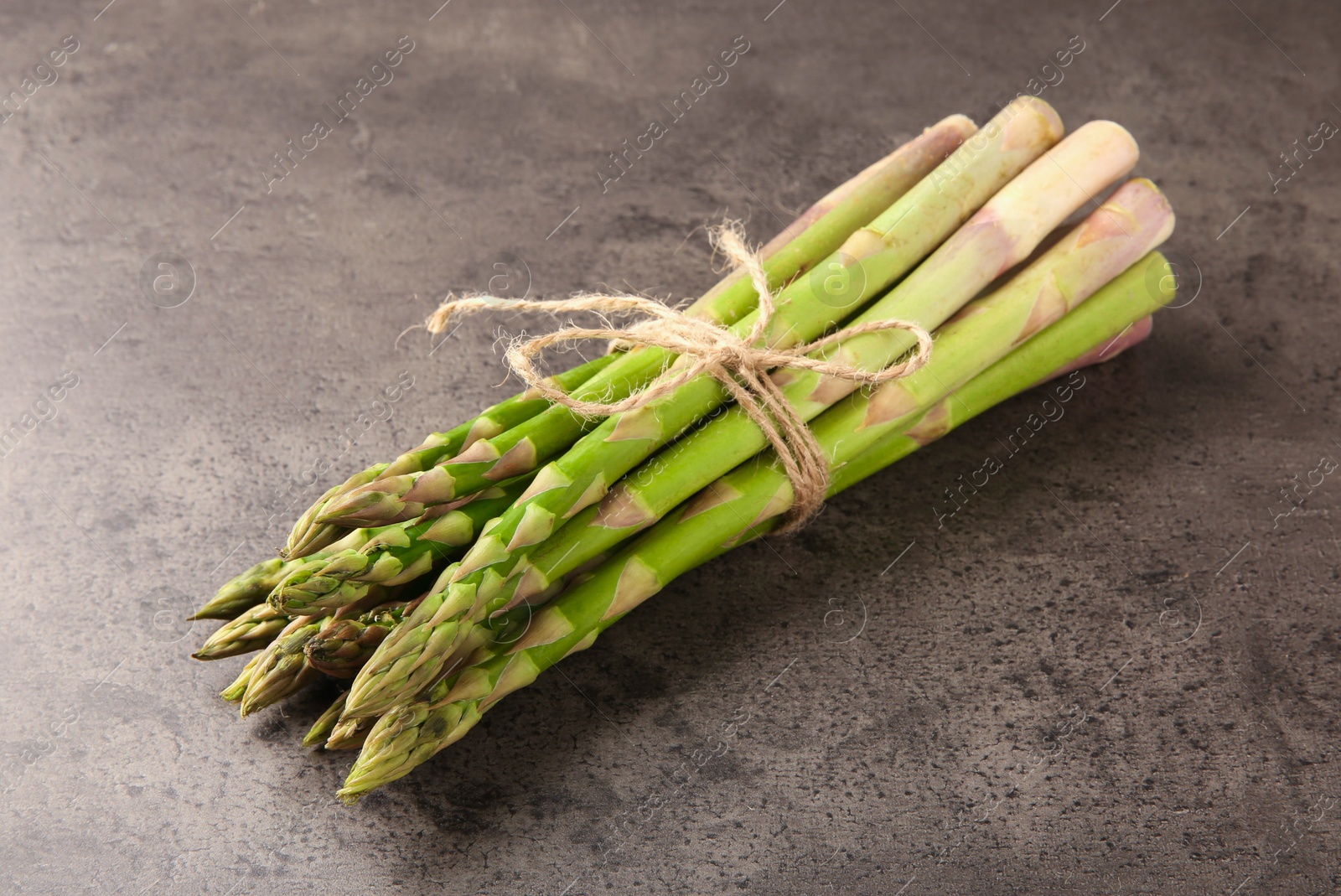 Photo of Bunch of fresh green asparagus stems on grey textured table, closeup