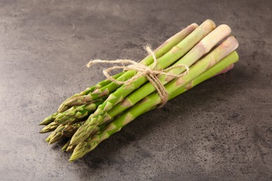 Photo of Bunch of fresh green asparagus stems on grey textured table, closeup