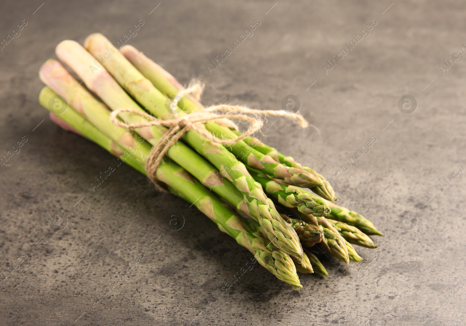 Photo of Bunch of fresh green asparagus stems on grey textured table, closeup