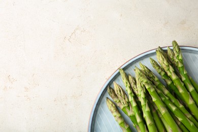 Photo of Plate with fresh green asparagus stems on light textured table, top view. Space for text