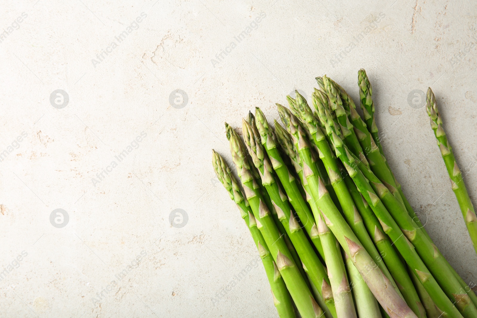 Photo of Many fresh green asparagus stems on light textured table, top view. Space for text