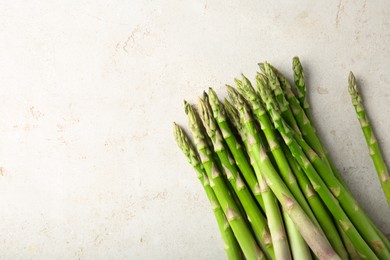 Photo of Many fresh green asparagus stems on light textured table, top view. Space for text