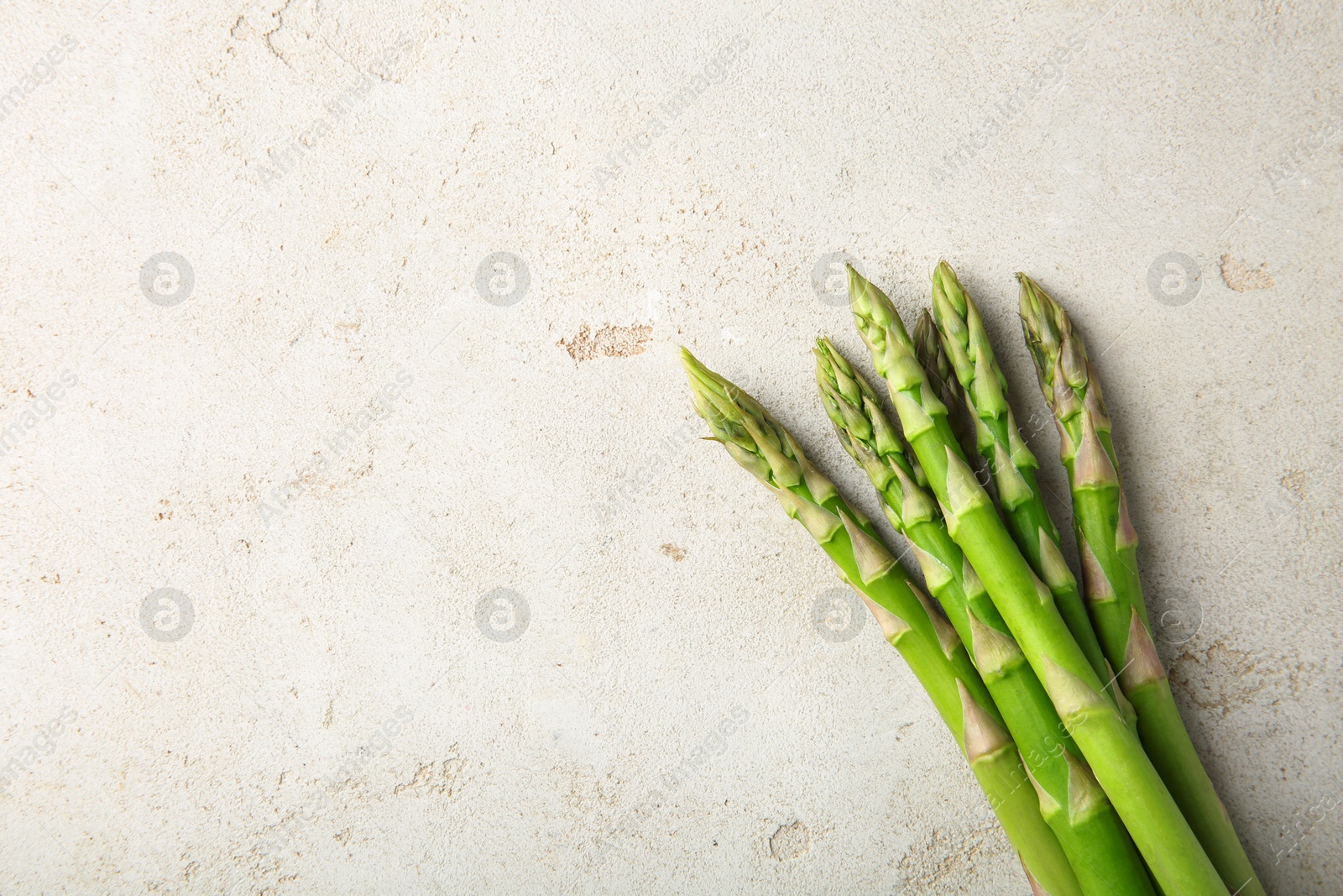 Photo of Many fresh green asparagus stems on light textured table, top view. Space for text