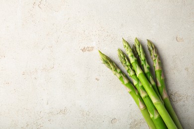 Many fresh green asparagus stems on light textured table, top view. Space for text