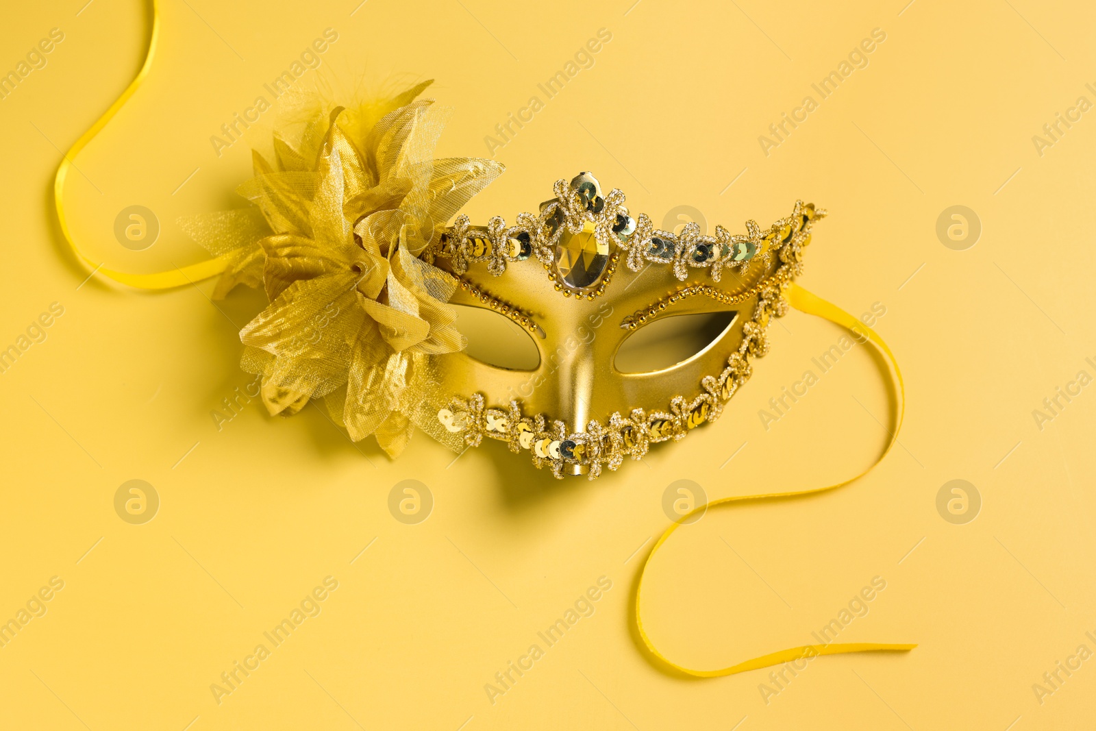 Photo of Beautiful carnival mask on yellow background, top view