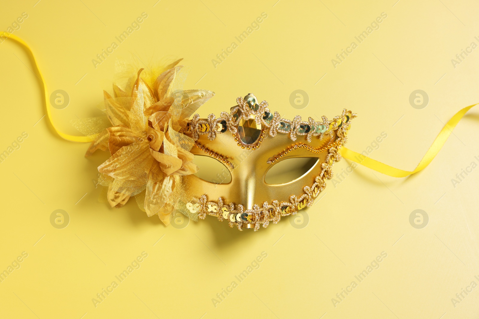 Photo of Beautiful carnival mask on yellow background, top view