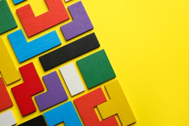 Colorful wooden puzzle pieces on yellow background, top view