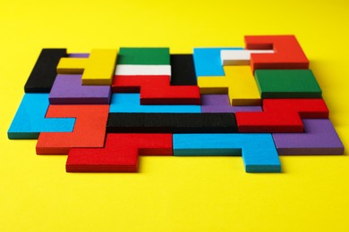 Photo of Colorful wooden puzzle pieces on yellow background, closeup