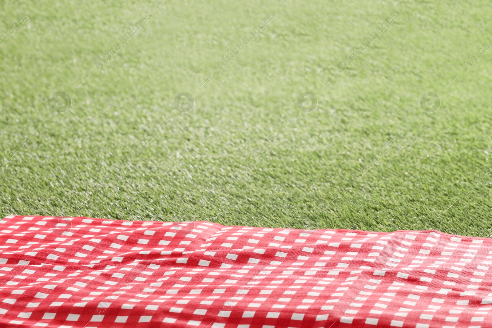 Photo of Checkered picnic tablecloth on green grass, closeup. Space for text