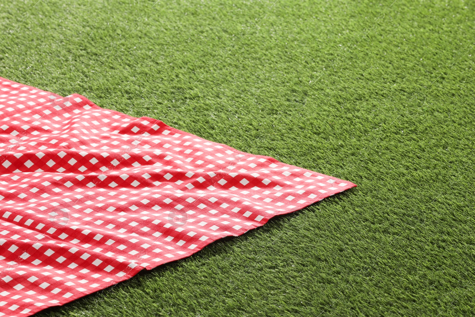 Photo of Checkered picnic tablecloth on green grass. Space for text