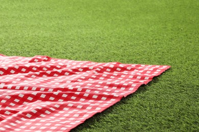 Photo of Checkered picnic tablecloth on green grass, closeup. Space for text