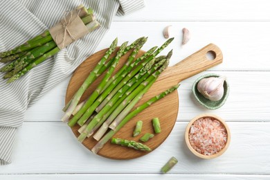 Fresh green asparagus stems, garlic and sea salt on white wooden table, flat lay