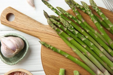 Photo of Fresh green asparagus stems and garlic on white wooden table, flat lay