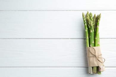 Photo of Bunch of fresh green asparagus stems on white wooden table, top view. Space for text