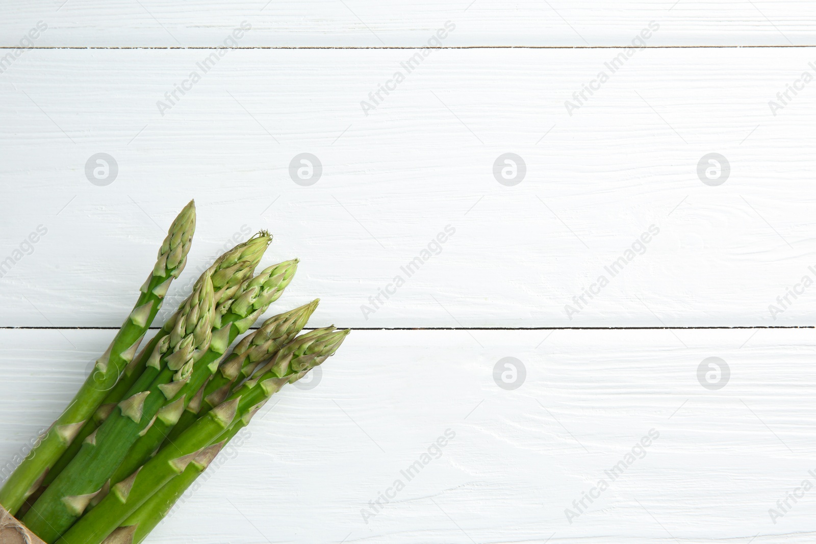 Photo of Fresh green asparagus stems on white wooden table, top view. Space for text