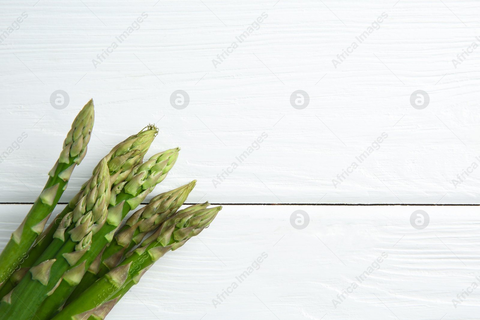 Photo of Fresh green asparagus stems on white wooden table, top view. Space for text