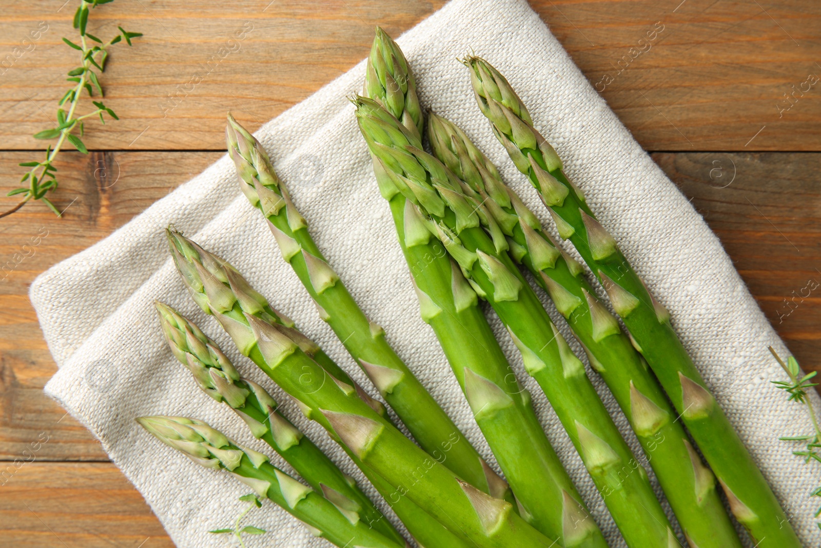 Photo of Fresh green asparagus stems and thyme on wooden table, top view