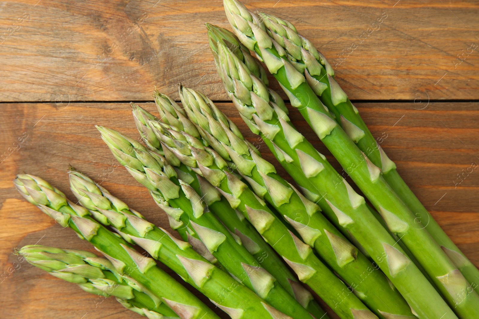 Photo of Fresh green asparagus stems on wooden table, top view