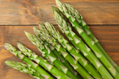 Photo of Fresh green asparagus stems on wooden table, top view